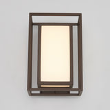 A modern wall sconce with a rectangular frosted glass shade, framed by a dark metal geometric structure, mounted on a light gray wall.