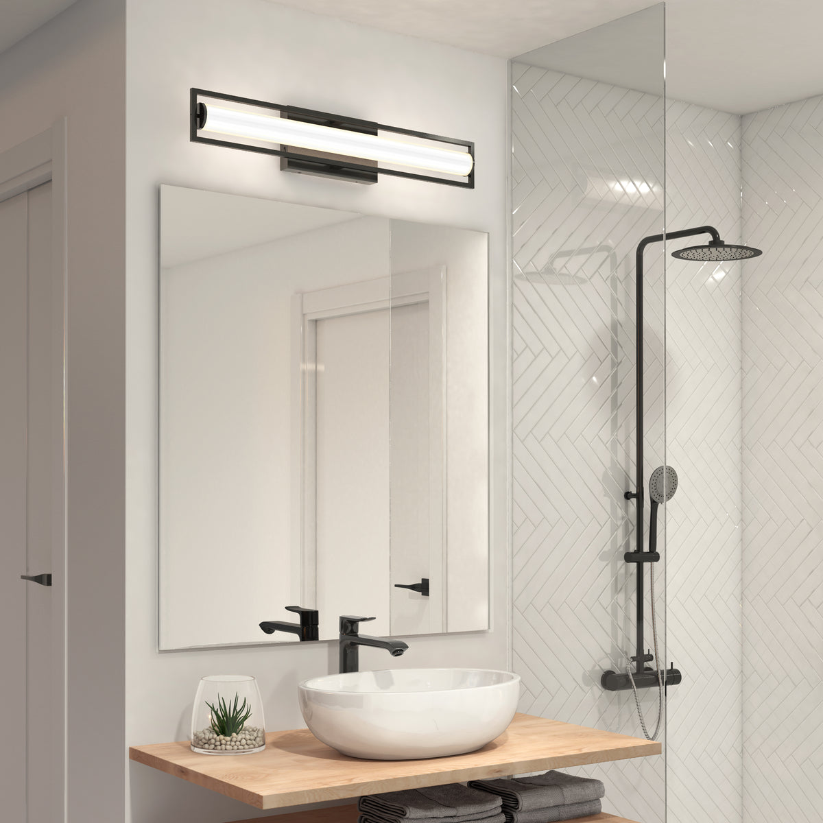 Modern bathroom with a round vessel sink, black faucet, and a small plant on a wooden countertop. A large mirror is above the sink, with a horizontal light fixture and a glass shower with black fixtures nearby.