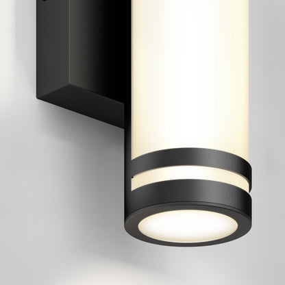 Close-up of the Artika Bradley modern LED indoor-outdoor wall light 3 CCT, featuring a black metal frame and frosted glass, mounted on a light-colored wall and emitting a soft, warm glow.