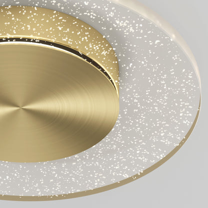 A close-up of the Essence Disk LED flush mount by Artika-CAN-dev shows its modern design with a circular brushed gold center and a translucent glass diffuser ring featuring sparkling bubble-like details.