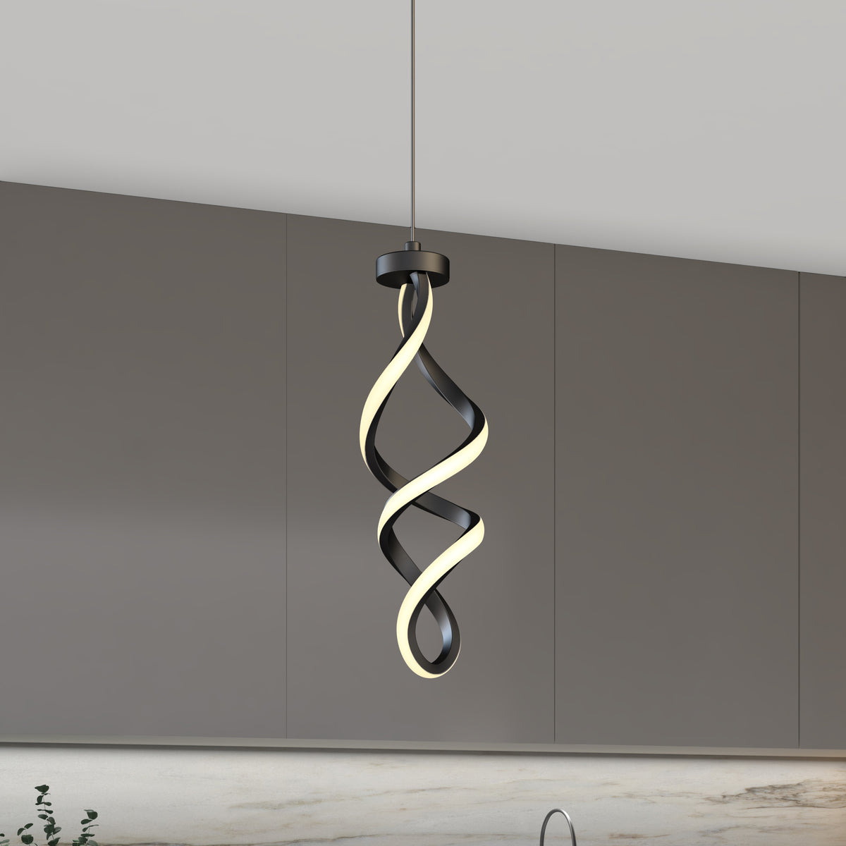 A modern pendant light with a twisted, spiral design hangs in front of gray kitchen cabinets and a light marble backsplash. The light features black and illuminated white elements intertwined.