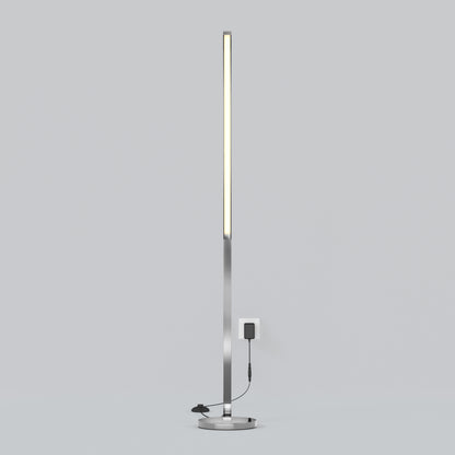 The Artika Arc LED Floor Lamp features a minimalistic, modern design with a slim vertical light on a round base, plugged into a wall outlet and set against a plain light gray background.