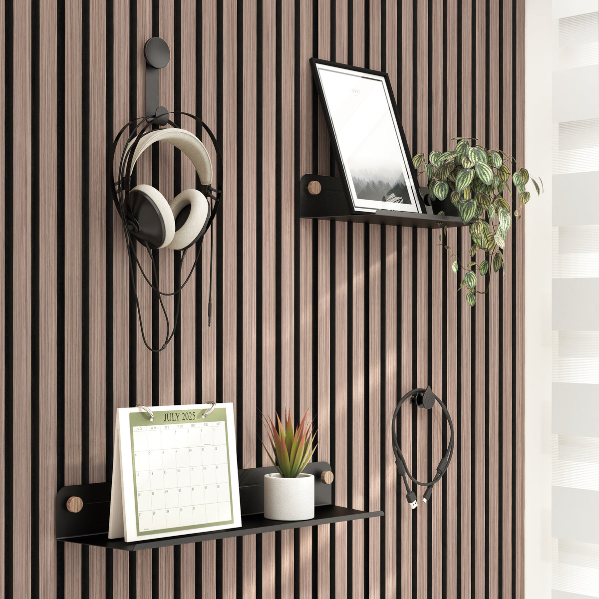 A modern slatted wood wall with two black shelves holding a framed photo, a potted plant, a small succulent, and a July 2023 calendar. Headphones and a charging cable hang from wall hooks. Light filters in from the right.