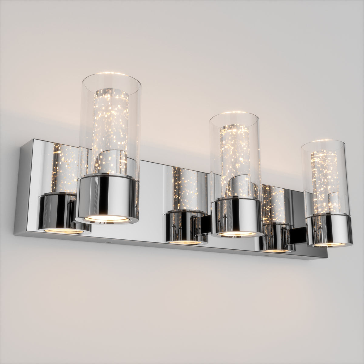 A modern wall-mounted light fixture with four cylindrical glass shades, each containing small bubbles, mounted on a shiny chrome rectangular base against a plain light-colored wall.