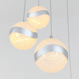 Three spherical pendant lights with textured, glowing surfaces and a diagonal metallic band hang from the ceiling against a plain, light background.