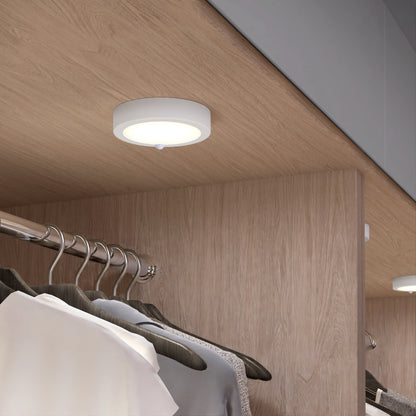 An Artika Accent under cabinet LED light 3CCT is mounted beneath a wooden shelf in a modern, wood-paneled closet, brightening clothes hanging on a metal rod below.