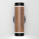 A modern wall sconce with a cylindrical wood finish body, black metal top and bottom edges, and white LED light strips at both ends, mounted on a circular black wall plate.
