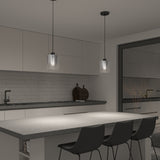 A modern kitchen with a gray island, three black chairs, white cabinets, subway tile backsplash, and two pendant lights hanging above the countertop. A black faucet and two cutting boards are visible near the sink.