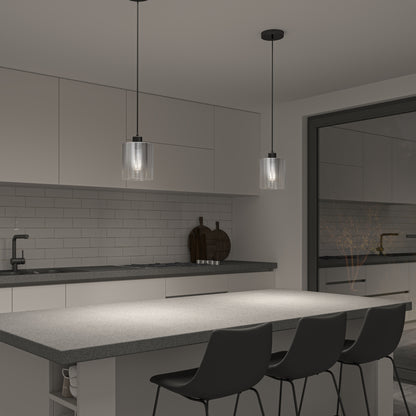 Modern kitchen with a gray island, three black chairs, white cabinets, and two Artika Haze glass pendant lights. Features a subway tile backsplash, sink, and large window showing another room.