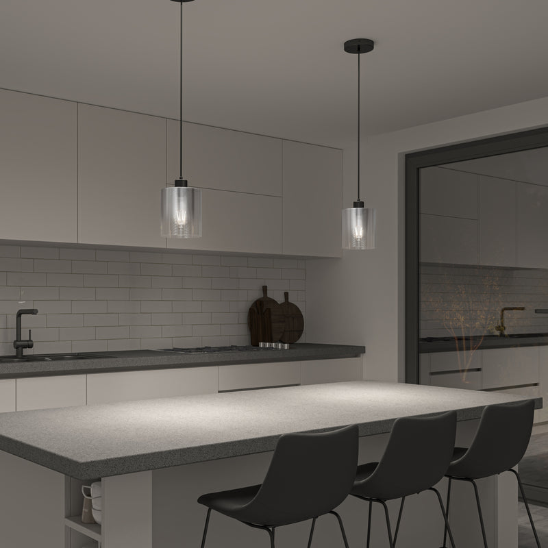 Modern kitchen with a gray island, three black chairs, white cabinets, and two Artika Haze glass pendant lights. Features a subway tile backsplash, sink, and large window showing another room.