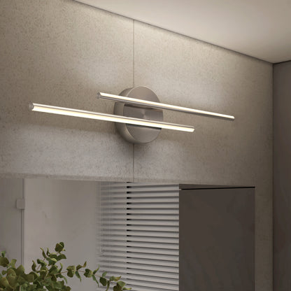 The Artika Cisco modern LED bathroom vanity light 5 CCT features two parallel horizontal LED bars on a round metal base, wall-mounted above a cabinet in a textured room with leafy green plants.