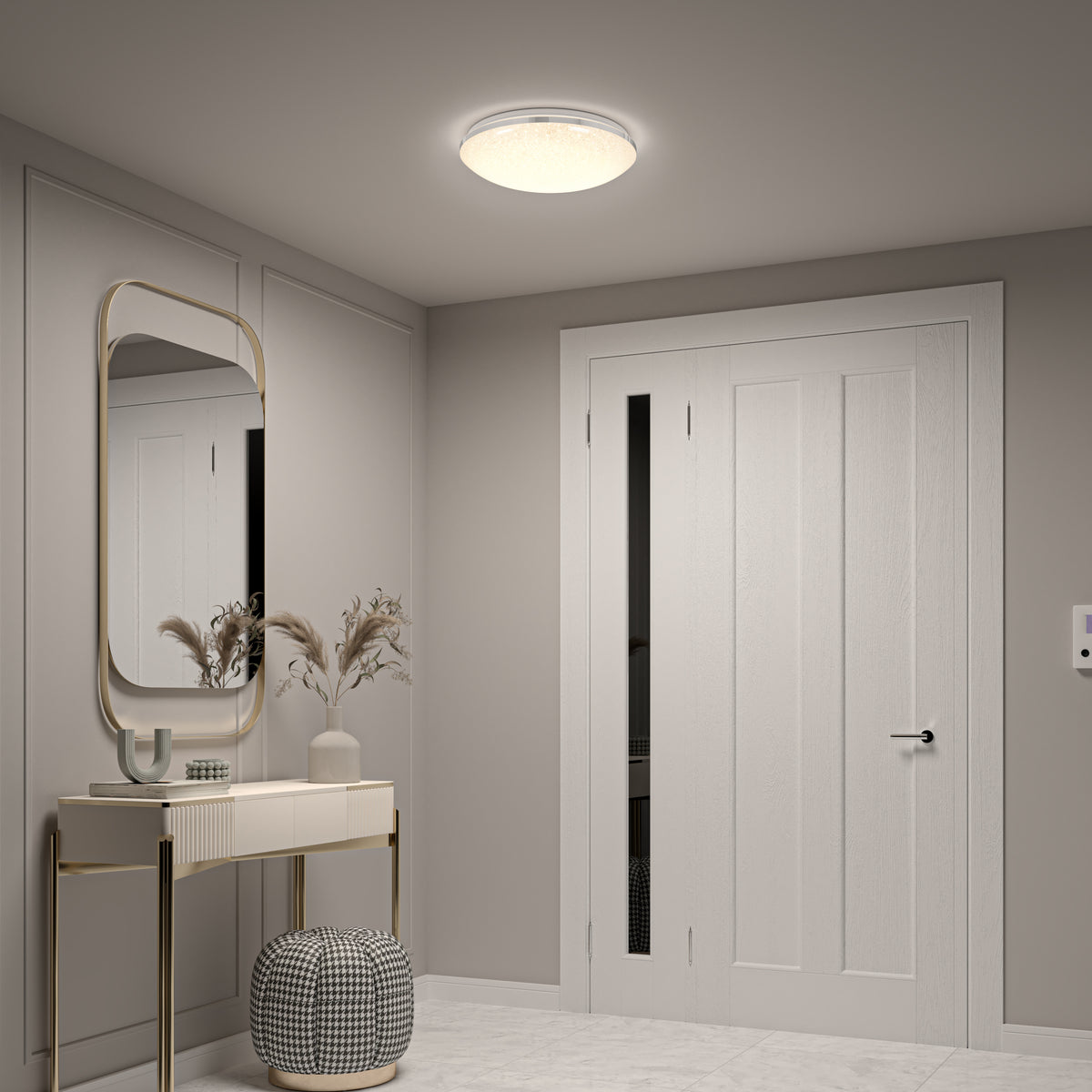 A modern hallway with a white door, a large wall mirror above a console table with decorative vases, and a patterned ottoman. The space is softly lit by a round ceiling light.