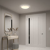 A modern hallway with a white door, a large wall mirror above a console table with decorative vases, and a patterned ottoman. The space is softly lit by a round ceiling light.