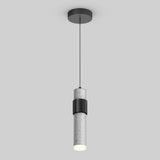 A modern cylindrical pendant light with a concrete finish, suspended by a thin black cord from a round ceiling mount. The light is illuminated, casting a soft glow downward.