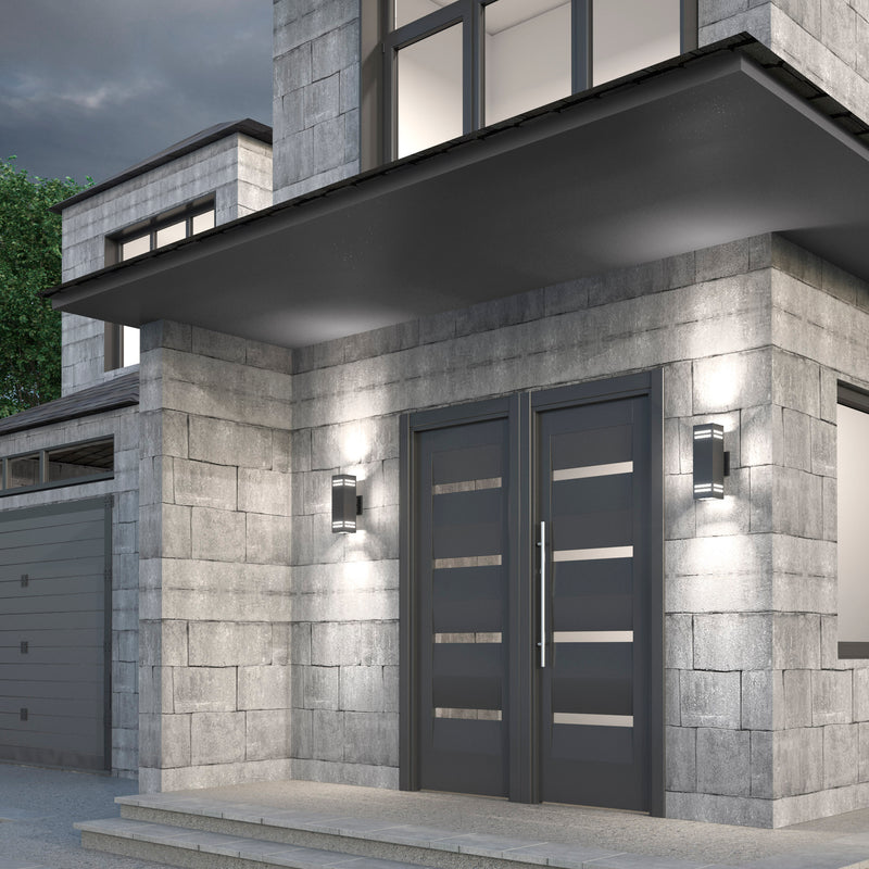 Modern house entrance with double gray doors and horizontal glass panels, flanked by Artika Strike indoor-outdoor wall lights. Light gray stone tiles cover the exterior, topped with a large overhang above the entryway.