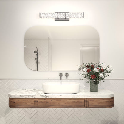 A modern bathroom with a white oval sink on a marble countertop, wooden drawers, a vase of flowers, a large mirror, and the Artika Royale LED bathroom vanity light above. Herringbone tile and a showerhead are in the background.