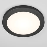 A round, modern ceiling light fixture with a black outer rim and a glowing white center, mounted on a white ceiling.