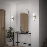A modern hallway with a black console table, a potted plant, stacked books, a decorative bowl, an arched mirror, wood doors, and two wall sconces with brass and glass accents.