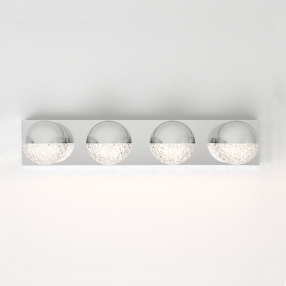 The Artika Carat LED bathroom vanity light is a modern wall-mounted fixture with four spherical lights featuring textured glass bottoms on a rectangular metallic base, shown against a white wall.
