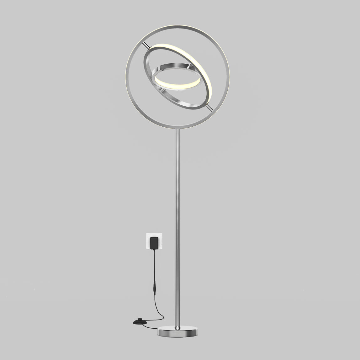 The Artika Pivot modern LED floor lamp 3 CCT features a sleek silver finish, circular elements, and an illuminated ring, shown plugged into a wall socket against a plain gray background.