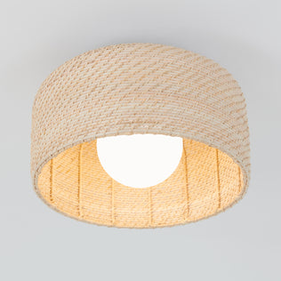 The Artika Emiko modern LED flush mount light 5 CCT features a woven beige rattan shade and a glowing white bulb in the center, all set against a light gray background.