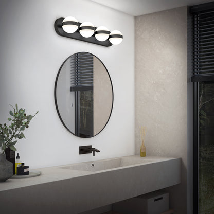 Modern bathroom featuring the Artika Baldric LED modern bathroom vanity light (3 CCT) above a round mirror, wall-mounted faucet, long sink, and minimal decor with a plant and toiletries. A window with blinds is on the right.