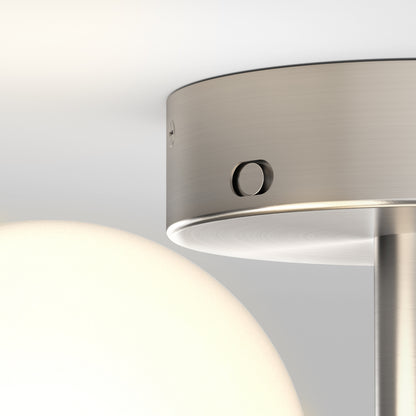 Close-up of the Artika Bloom LED flush mount, showcasing its modern brushed metal fixture, round white glass shade, and small round switch on the metal surface.