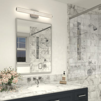 Modern bathroom with marble walls and countertop, a large mirror above a dark vanity, a glass shower, a small flower arrangement, and an Artika Exalto LED bathroom vanity light mounted on the wall above the counter.