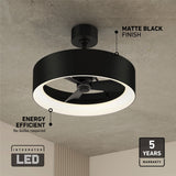 Ceiling fan with a matte black finish and integrated LED light, mounted on a beige ceiling. Text highlights energy efficiency, no bulbs required, and a 5-year warranty. Modern, circular design.