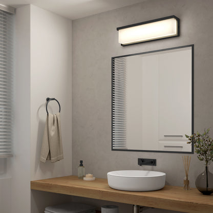 Modern bathroom featuring a round white vessel sink on a wood counter, black-framed mirror, Artika Bristol modern LED bathroom vanity light (3 CCT) above the mirror, beige towel on a ring, and small decorative items on the counter.