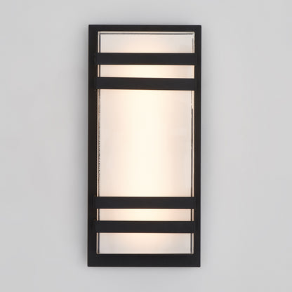 The Artika Glowbox 3 indoor-outdoor LED wall light features a rectangular design with frosted glass, a black metal frame, and two horizontal black bars. It emits a soft glow through the center glass panel.