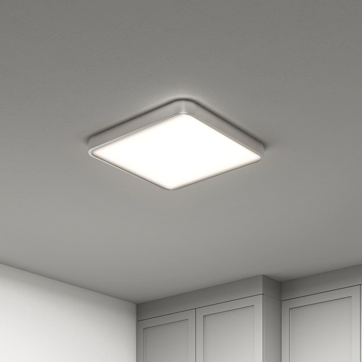 The Artika Europa 18 in. LED flush mount light, featuring a sleek silver frame, is illuminated on a smooth white ceiling above light-colored cabinets, with remote control included.