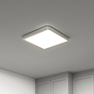 The Artika Europa 18 in. LED flush mount light, featuring a sleek silver frame, is illuminated on a smooth white ceiling above light-colored cabinets, with remote control included.