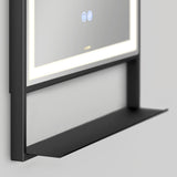 A close-up of a sleek, modern wall-mounted mirror with built-in LED lighting and a black metal shelf below it on a light gray wall.