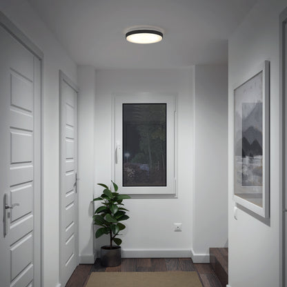 A modern, white hallway with three closed doors, a window at the end above a potted plant, a framed picture on the right wall, dark wooden flooring, and an Artika Sunraker 10 in. LED modern flush mount ceiling light.