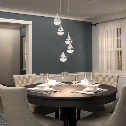 A modern dining room features a round dark wood table for four, beige upholstered chairs, and the Artika Glitzer 5-light LED pendant overhead. Blue-gray walls and sheer white curtains let in sunlight through the window.