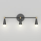 A modern wall sconce with three black and gold cone-shaped light fixtures, each holding a round white bulb, mounted on a flat, light gray wall.