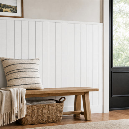 Wooden bench with striped pillow and blanket sits by Artika AXEN Shilap MDF wall panels in a bright entryway with basket and black door.