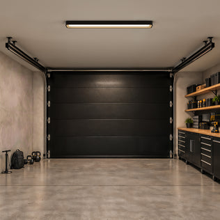 An Artika Alton 48 in. x 6 in. Modern Ceiling Light 5 CCT is centered on the ceiling of a garage with a black door and storage cabinets.