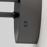 Close-up view of a modern, black, wall-mounted cylindrical light fixture attached to a white wall, featuring a small round button on its side.