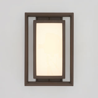 The Artika Ghost indoor-outdoor LED wall light features a frosted panel framed by a dark metal border, mounted on a light gray wall.