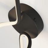 Close-up of a modern ceiling light fixture with a black base and curved, illuminated white light strips attached to it, set against a white ceiling.