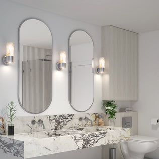 Modern bathroom featuring two oval mirrors, a marble countertop with dual sinks, Artika Marble LED contemporary sconces, silver fixtures, potted plants, light wood cabinetry, and a toilet with toilet paper on the right.