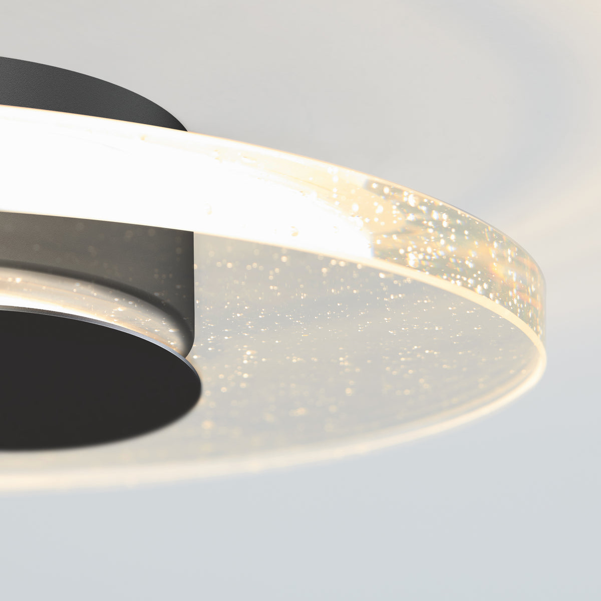 Close-up of a modern ceiling light fixture with a circular, translucent ring featuring embedded bubbles and glowing edges, attached to a black base against a light background.