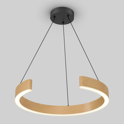 A modern ceiling pendant light with a black round base and three supporting cables holding a circular, partially open wooden ring that emits a soft, white glow. The background is plain light gray.