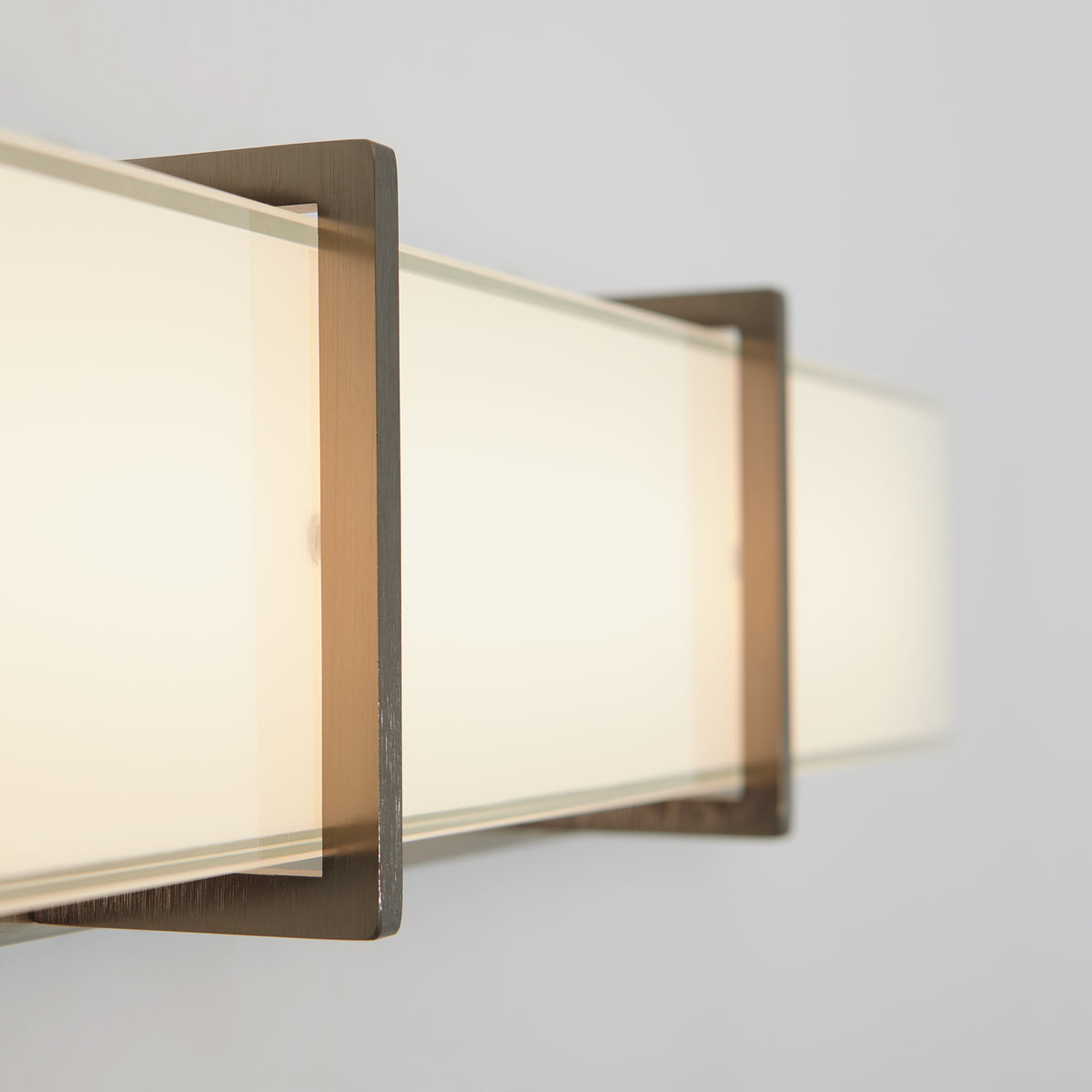 Close-up of a modern wall-mounted rectangular light fixture with frosted glass and metal frame, emitting a soft, warm glow against a light-colored wall.