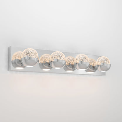 The Artika Oracle LED bathroom vanity light features five round glass and chrome bulbs on a sleek rectangular chrome base, casting a soft glow against the wall.