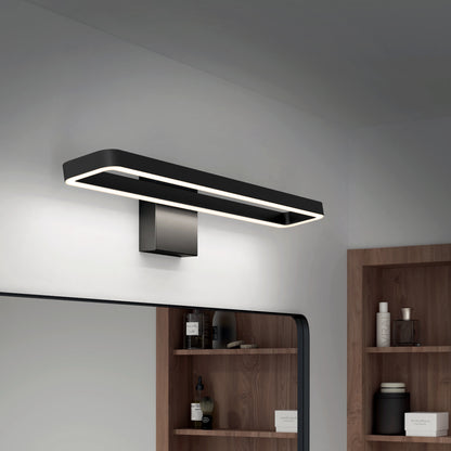 The Artika Hinge LED modern bathroom vanity light 3 CCT in black is mounted above a mirror in a minimalist bathroom with wooden shelves displaying toiletries and decor.