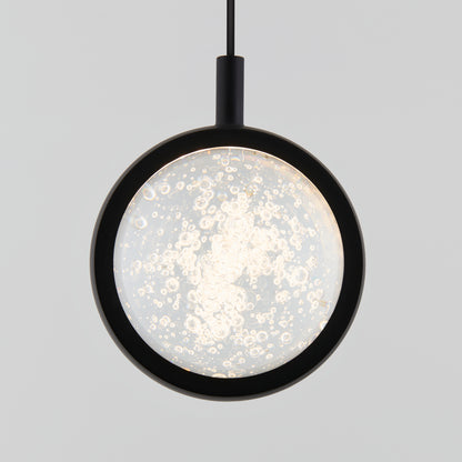 The Avalon LED 1-light pendant by Artika features a modern circular black frame and an illuminated glass center filled with bubbles, creating a shimmering decorative effect against any plain background.