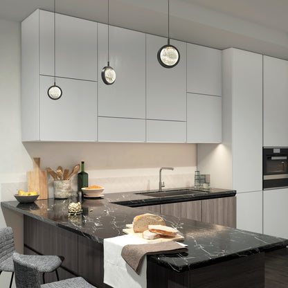 A modern kitchen features white cabinets, a black marble island countertop, three Artika Avalon LED 1-light pendants, and kitchen items like bread, olive oil, wooden utensils, and a built-in oven.